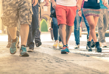Crowd of people walking on the street - Detail of legs and shoes moving on sidewalk in city center - Travellers with multicolor clothes on vintage filter - Shallow depth of field with sunflare halo - obrazy, fototapety, plakaty