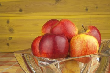 Red apples in a glass bowl on the kitchen table. Healthy food on the table. Autumn harvest of apples. Vitamins and fiber snack for children. Diet for athletes.
