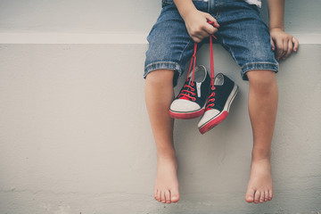 Little boy  sitting near the house and keeping the youth sneaker