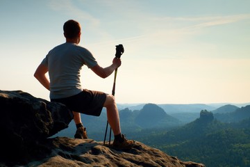 Tired sitting tourist with poles in hand. Sunny spring daybreak in rocky mountains. Hiker with...