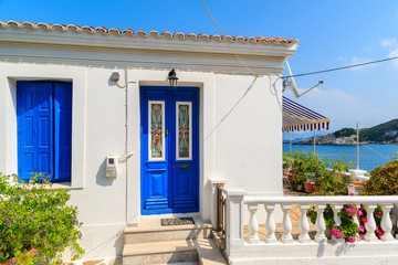 Fototapeta na wymiar Typical white Greek house with blue door and window in Kokkari town on coast of Samos island, Greece