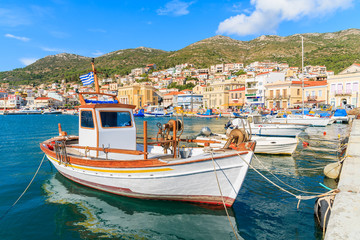 Fototapeta na wymiar Traditional Greek boat in port of Samos with colourful houses in background, Greece