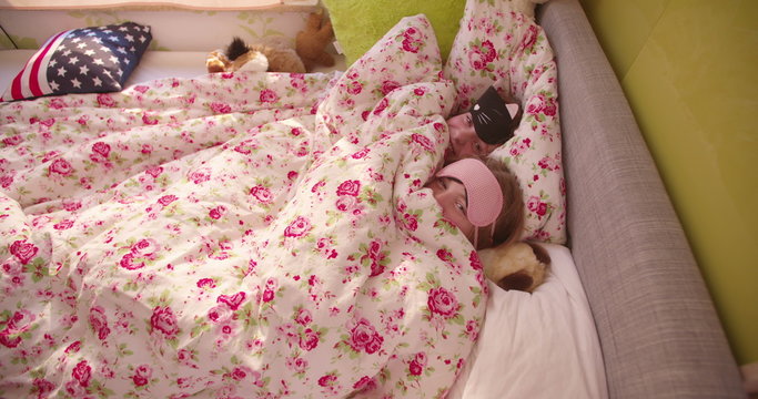 Adolescent girls hiding under the bed covers with sleeping masks