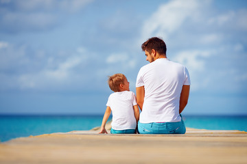 happy father and son sitting on pier and talk