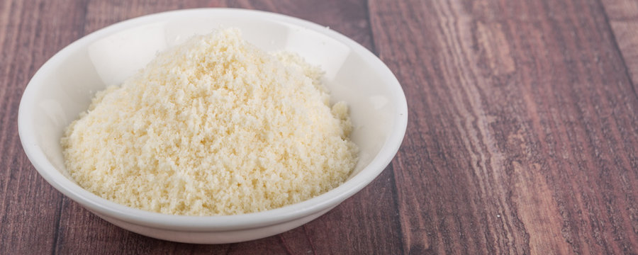 Grated cheese in white bowl over wooden background