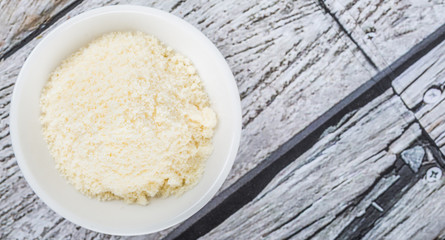 Grated cheese in white bowl over wooden background