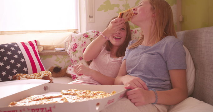 Girl laughing and feeding her friend pizza in bed