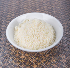 Grated cheese in white bowl over wicker background