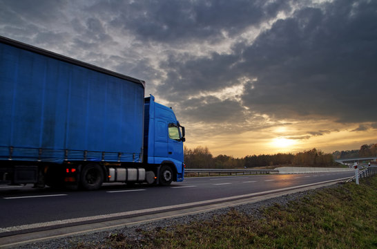 Blue truck on highway at sunset in the countryside. Dark clouds in the sky.