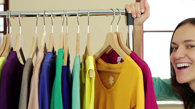 Young smiling woman pushing a movable rack of clothes, slow motion