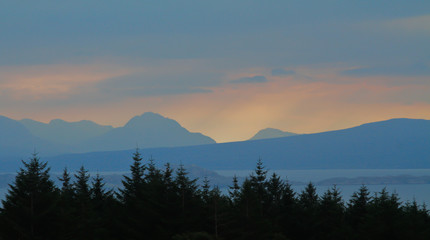 Sunrise over sihouetted trees with mountains in background 