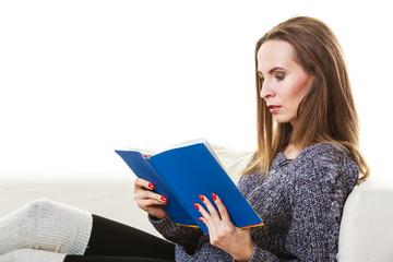 Woman sitting on couch reading book at home