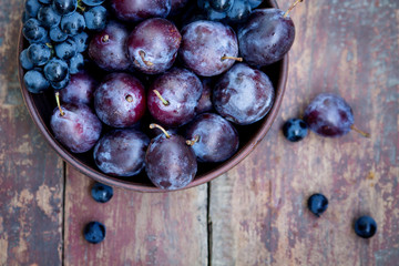 Plums and grapes in a bowl on the wooden table