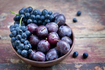 Plums and grapes in a bowl on the wooden table