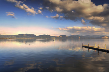 Wooden pier or jetty and on a blue lake sunset and sky reflectio