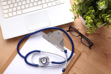 A medical stethoscope near a laptop on a wooden table, on white