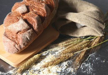 rustic crusty bread and wheat ears on a dark wooden table