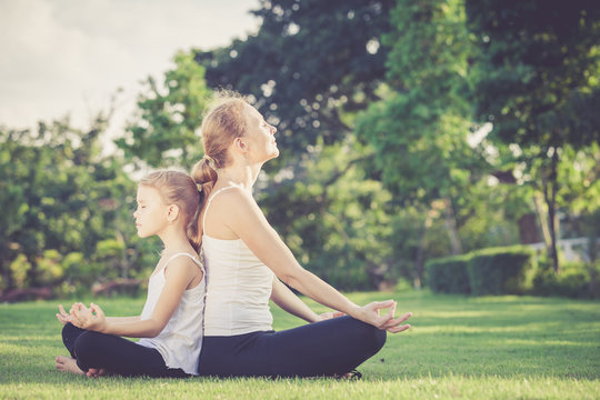 Mother and daughter doing yoga exercises on grass in the park.