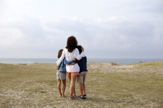 Madre e hijos abrazados mirando el mar