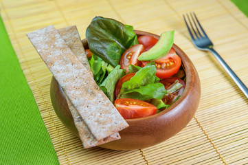 Fresh vegetable salad in wooden bowl on bamboo napkin with crispbread