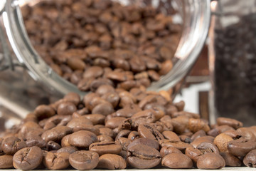 Close-up of roasted coffee beans that get out of an overturned and open glass jar