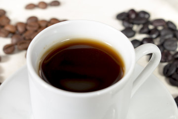 Detail view of coffee cup beside natural roasted and torrefacto coffee beans, on a white table