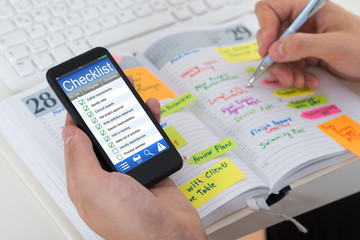 Person Checking List From Mobile Phone And Diary