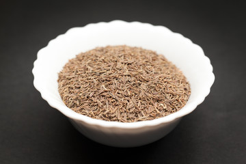 Organic Caraway (Carum carvi) in white ceramic bowl on dark background.