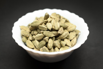 Organic Green or True cardamom (Elettaria cardamomum) in white ceramic bowl on dark background.