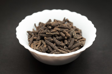 Organic Long pepper Dried Fruit (Piper longum) in white ceramic bowl on dark background.
