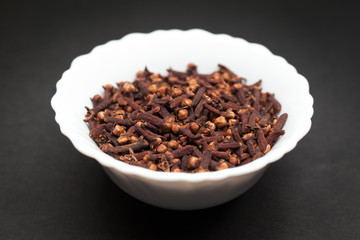 Organic black clove (Syzygium aromaticum) in white ceramic bowl on dark background.