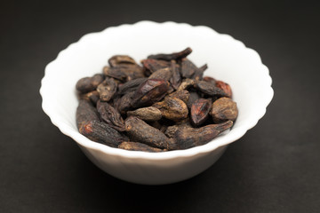 Organic Chebulic Myrobalan or Choti Harad (Terminalia chebula) in white ceramic bowl on dark background.