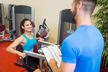 Fototapeta na wymiar Smiling woman on weights machine beside trainer
