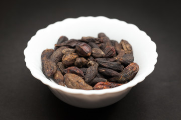 Organic Chebulic Myrobalan or Choti Harad (Terminalia chebula) in white ceramic bowl on dark background.