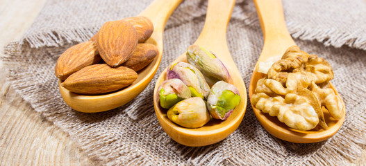 Almonds, walnuts and pistachio on a wooden spoon.