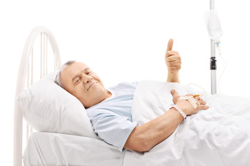 Senior patient lying in hospital bed and giving thumb up
