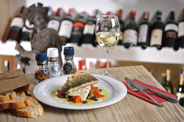Grilled fish and garnitures in plate and white wine on wooden table