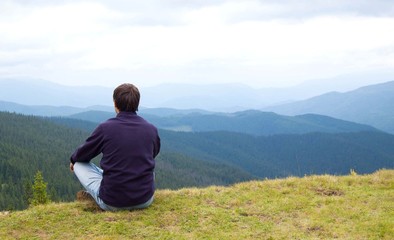 Fototapeta na wymiar Tourist sits and looks at mountains landscape
