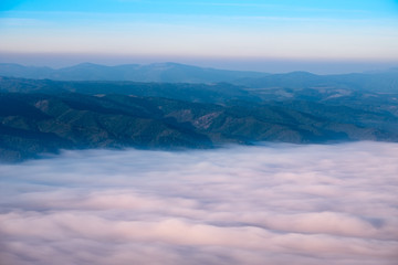 Fototapeta na wymiar Autumn landscape view of mountain hills above misty clouds at su