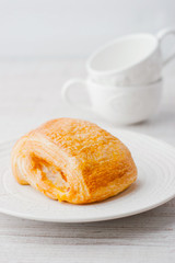 Cream puff on the white plate with two blurred cup at the right