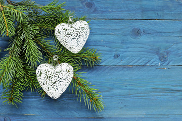 Christmas tree branch with glass hearts on blue wooden background 