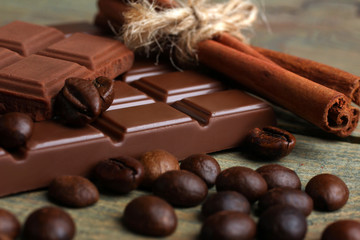 tender milk chocolate and cinnamon with coffee beans on wooden background