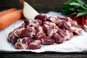 Raw Duck hearts on crumpled paper, decorated with vegetables. on old wooden table.