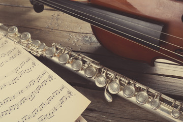 Flute and violin with music notes on wooden table close up