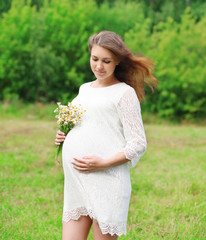 Fototapeta na wymiar Beautiful young pregnant woman with chamomiles flowers outdoors
