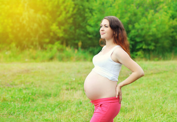 Fototapeta na wymiar Happy fitness pregnant smiling woman enjoys sunny summer day
