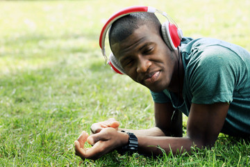 Handsome African American man with headphones lying on green grass