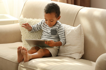 Little boy sitting on sofa with tablet in the room