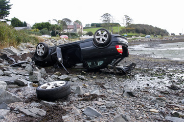 Crashed car lying on roof at seashore