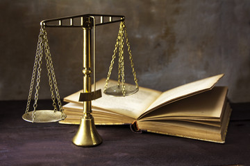Vintage brass scales of justice and an old book on a brown woode